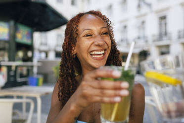 Fröhliche junge Frau stößt in einem Straßencafé mit Gläsern an - DCRF01425