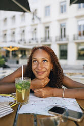 Lächelnde Frau mit Hand am Kinn, die sich an einen Tisch lehnt - DCRF01429