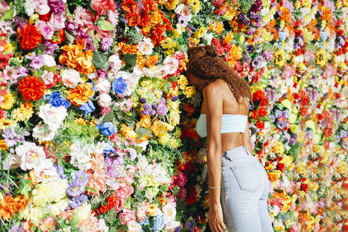 Junge Frau mit lockigem Haar lehnt ihren Kopf an eine Blumenwand - DCRF01445