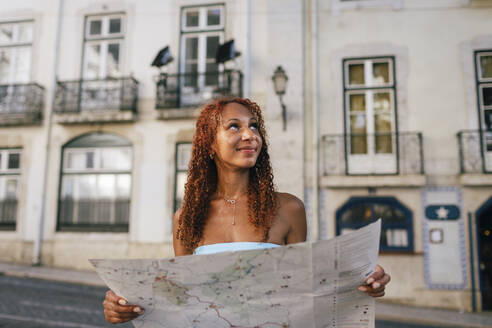 Lächelnde junge Frau mit Landkarte vor einem Gebäude sitzend - DCRF01451
