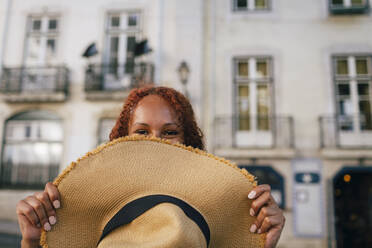 Frau, die ihr Gesicht mit einem Hut bedeckt, vor einem Gebäude - DCRF01454
