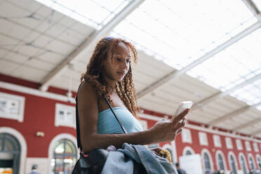 Woman using smart phone standing at railroad station - DCRF01467