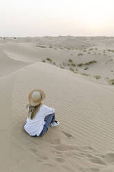 Woman wearing hat sitting on sand at desert - TYF00424