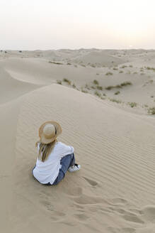 Frau mit Hut sitzt auf Sand in der Wüste - TYF00424