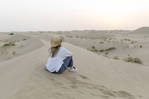 Frau mit Hut sitzt auf Sand in der Wüste bei Sonnenuntergang - TYF00425