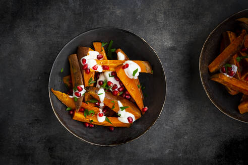 Studio shot of two bowls of sweet potatoes with parsley, pomegranate seeds and yogurt sauce - LVF09245