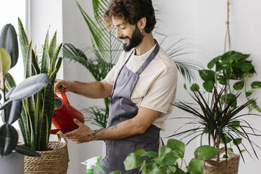 Lächelnder Mann beim Gießen von Pflanzen aus einer Gießkanne in einem Pflanzengeschäft - XLGF03082