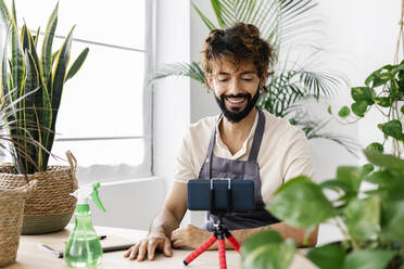 Happy man with mobile phone on tripod at plant shop - XLGF03092