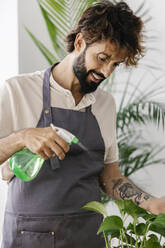 Smiling man spraying water on plant at shop - XLGF03102