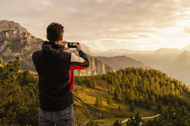 Mann fotografiert Berg durch Smartphone bei Sonnenuntergang - DIGF18754