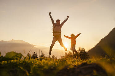 Mann mit Tochter springt bei Sonnenuntergang auf den Berggipfel - DIGF18811