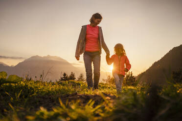 Smiling woman holding daughter's hand walking on mountain - DIGF18816