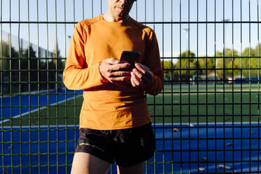 Sportler hält Handy vor einem Zaun - ASGF02895