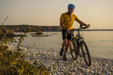 Glücklicher reifer Mann, der mit dem Fahrrad am Strand spazieren geht - UUF27222