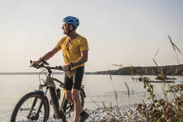 Man wearing cycling helmet walking with bicycle at beach - UUF27223