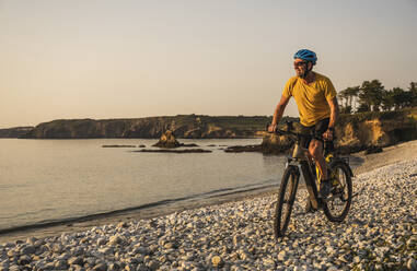 Älterer Mann genießt Fahrradfahren am Meer bei Sonnenuntergang - UUF27225