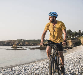 Man wearing cycling helmet riding bicycle at beach - UUF27228