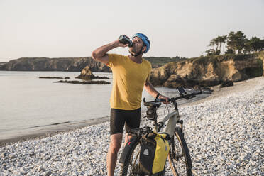 Mature man with bicycle drinking water at beach - UUF27231