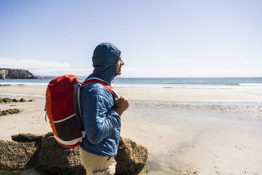 Mann mit Rucksack steht am Strand an einem sonnigen Tag - UUF27244