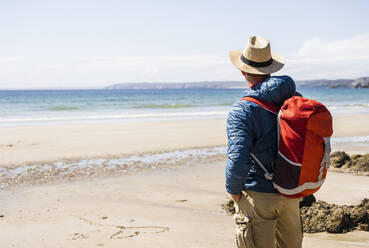 Mann mit Rucksack bewundert das Meer am Strand - UUF27247