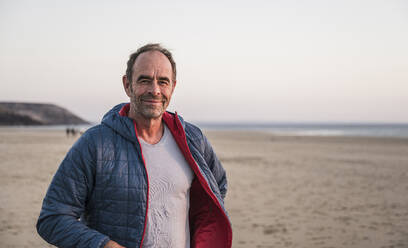 Lächelnder Mann mit Jacke vor dem Himmel am Strand - UUF27274