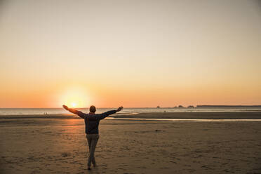 Mann mit ausgestreckten Armen genießt am Ufer bei Sonnenuntergang - UUF27278