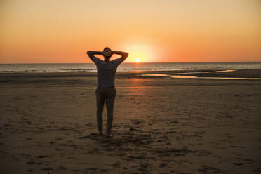 Man with hands behind head on shore at sunset - UUF27281