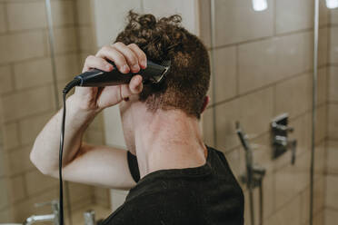 Junger Mann beim Rasieren der eigenen Haare im Badezimmer zu Hause - YTF00095