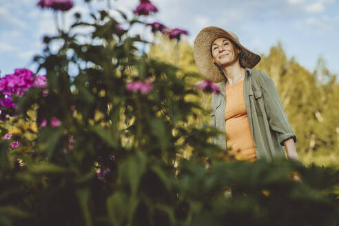 Lächelnde Frau mit Hut träumt im Garten - IEF00051