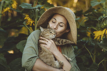 Ältere Frau küsst getigerte Katze im Garten - IEF00081