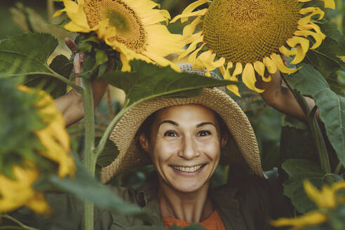 Glückliche Frau inmitten von Sonnenblumen im Garten - IEF00089