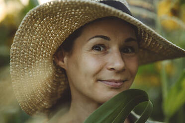 Smiling woman with hat in garden - IEF00100