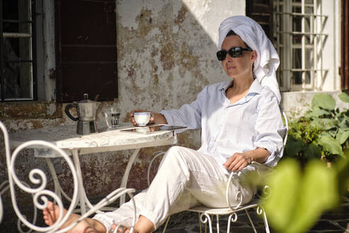 Mature woman with sunglasses having coffee on terrace - DIKF00705