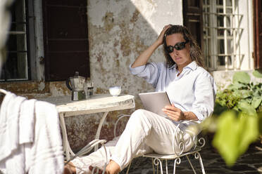 Reife Frau mit Hand im Haar, die auf dem Dach einen Tablet-PC benutzt - DIKF00709