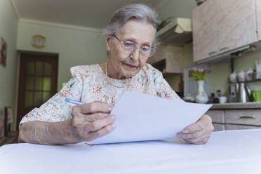 Senior woman with eyeglasses reading paper document at home - OSF00955