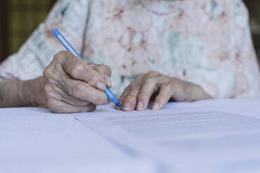 Ältere Frau beim Unterschreiben von Versicherungspapieren zu Hause - OSF00959
