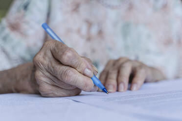 Die faltige Hand einer älteren Frau, die zu Hause einen Vertrag unterschreibt - OSF00960