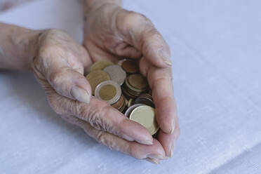 Senior woman holding coins in cupped hands on table - OSF00974