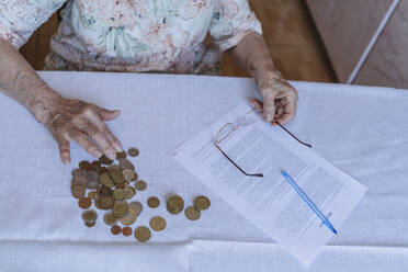 Ältere Frau zählt Münzen durch Vereinbarung Papiere auf dem Tisch zu Hause - OSF00982