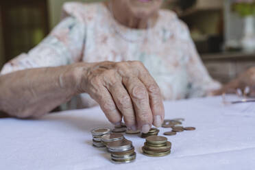 Ältere Frau stapelt Münzen auf dem Tisch zu Hause - OSF00988