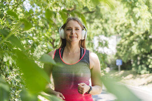 Lächelnde Frau mit drahtlosen Kopfhörern beim Joggen im Park - OSF00998