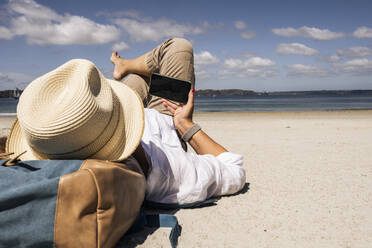 Ältere Frau benutzt ihr Smartphone und entspannt sich am Strand an einem sonnigen Tag - UUF27285