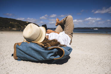 Mature woman wearing hat using smart phone lying at beach - UUF27286