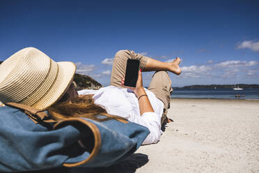 Reife Frau entspannt sich und benutzt ihr Smartphone am Strand - UUF27287