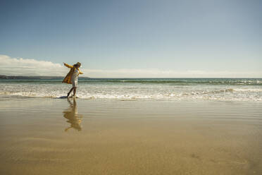 Mature woman with arms outstretched walking on shore at beach - UUF27303