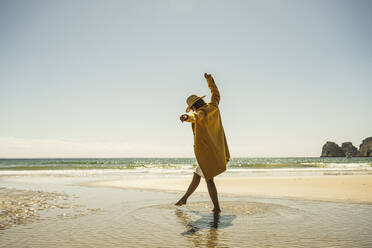 Ältere Frau mit erhobenen Armen genießt den Urlaub am Strand an einem sonnigen Tag - UUF27305