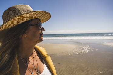 Ältere Frau mit Hut und Sonnenbrille am Strand an einem sonnigen Tag - UUF27309