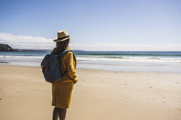 Reife Frau mit Rucksack am Strand stehend an einem sonnigen Tag - UUF27310