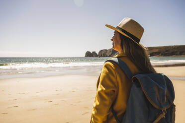 Frau mit Rucksack am Strand stehend an einem sonnigen Tag - UUF27311