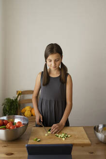 Mädchen schneidet Gemüse und sieht sich zu Hause ein Tutorial auf einem Tablet-PC an - LESF00265